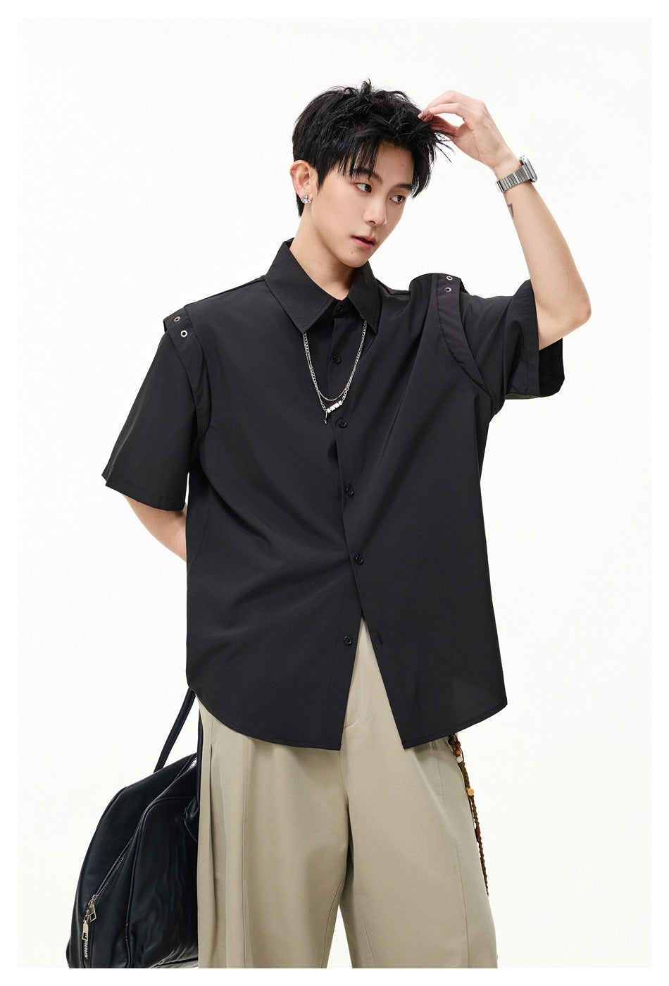 Model wearing a black short-sleeve button-up shirt with metal-eyelet shoulder tabs and beige wide-leg trousers.