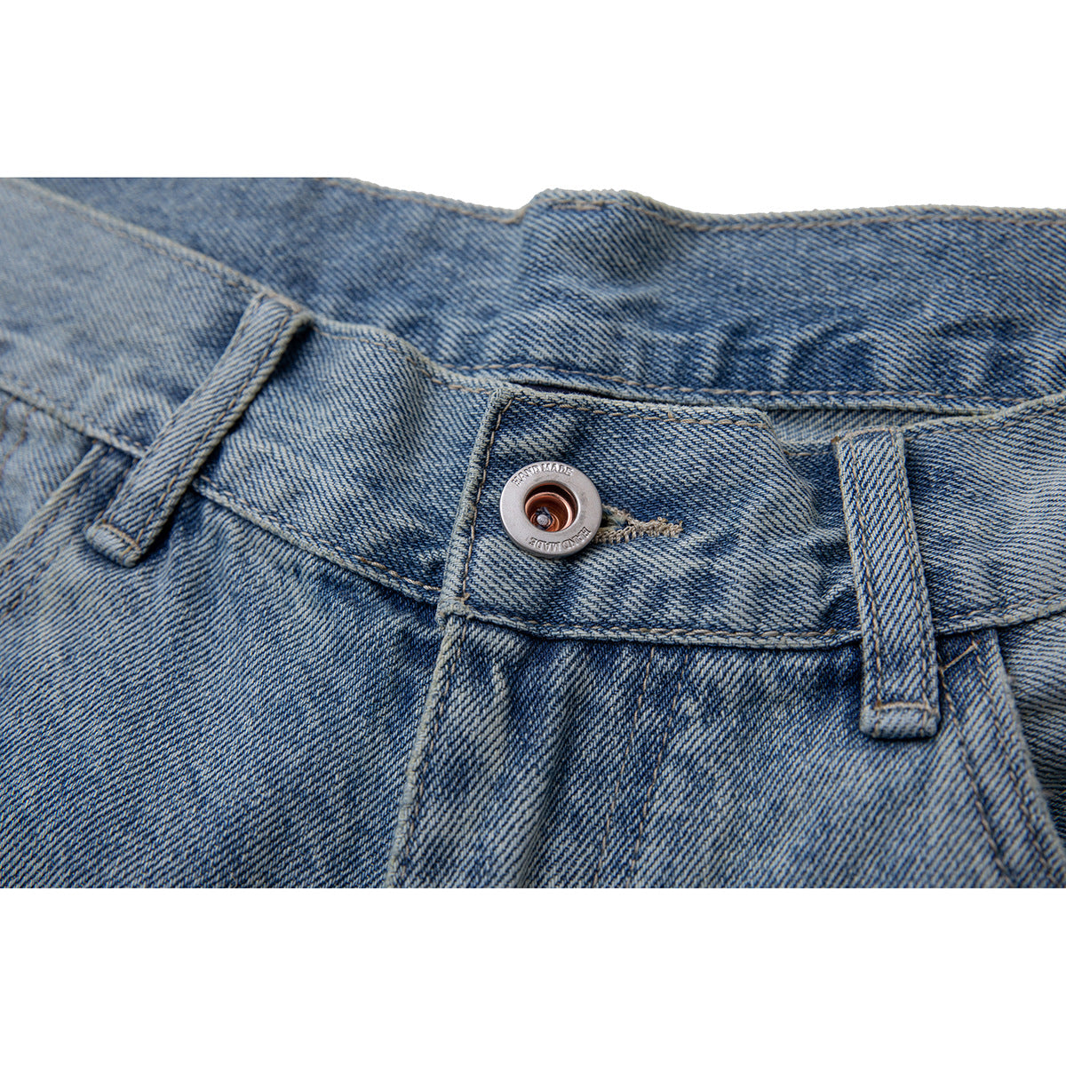 Close-up of the waistband and metal button on light blue washed jeans.