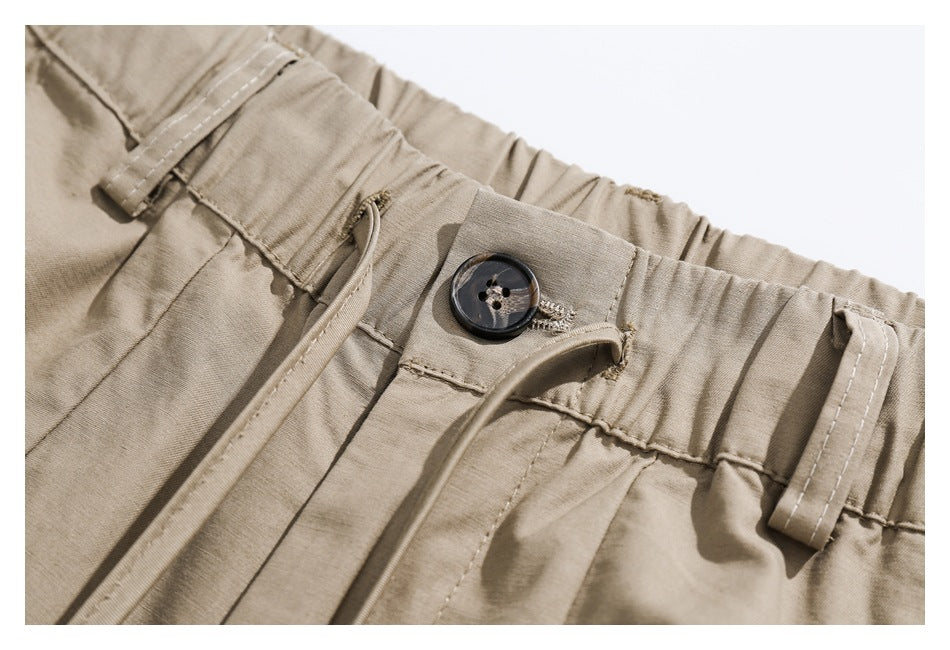 Close-up of beige pants showing an elastic waistband, belt loops, button closure, and drawstring.