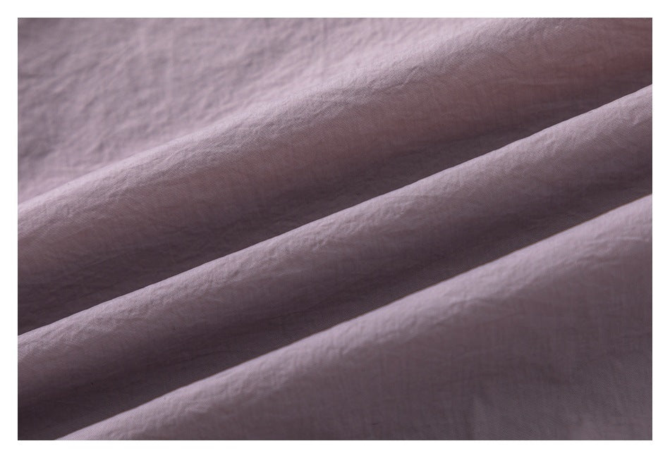 Close-up of muted mauve-gray fabric folded into diagonal ridges, showing its fine surface texture.