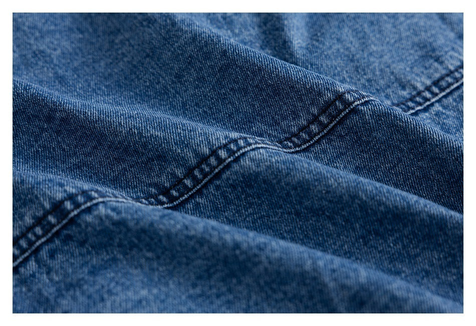 Close-up of blue denim with diagonal folds and dark double-stitched seams.