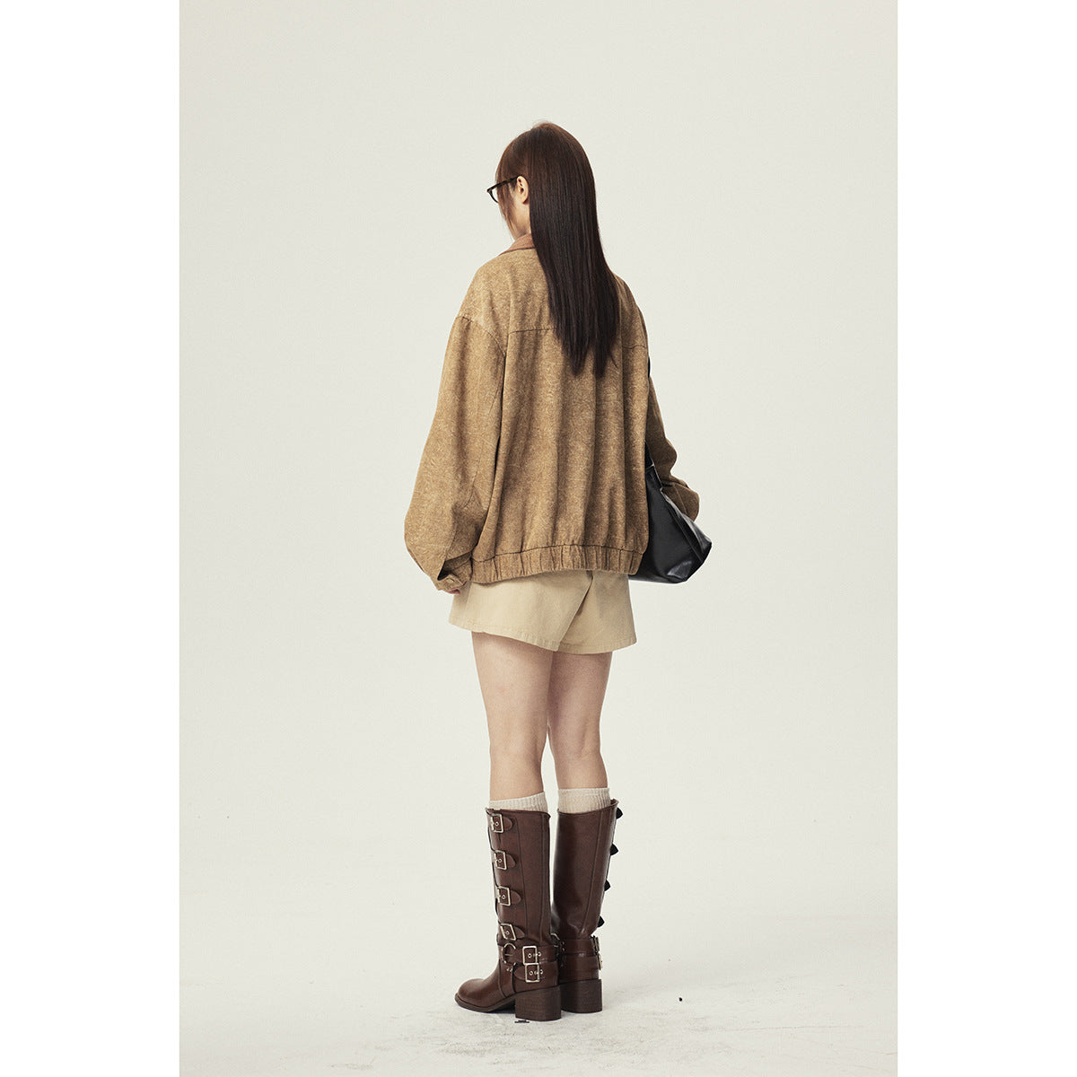 Back view of a model wearing an oversized tan jacket, beige shorts, and tall brown boots.
