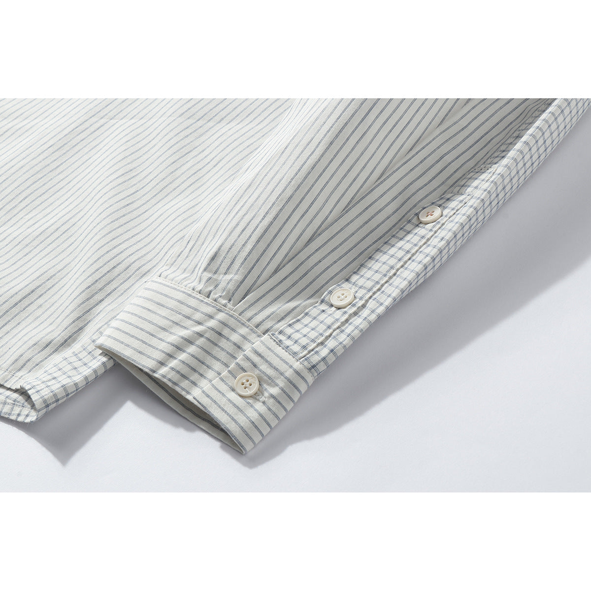 Close-up of the striped shirt's buttoned cuff and sleeve placket, with checked trim along the edge.