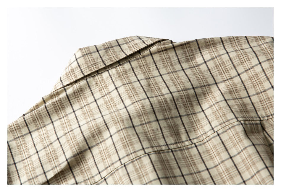 Close-up of a beige plaid shirt collar and upper shoulder with dark brown grid lines.