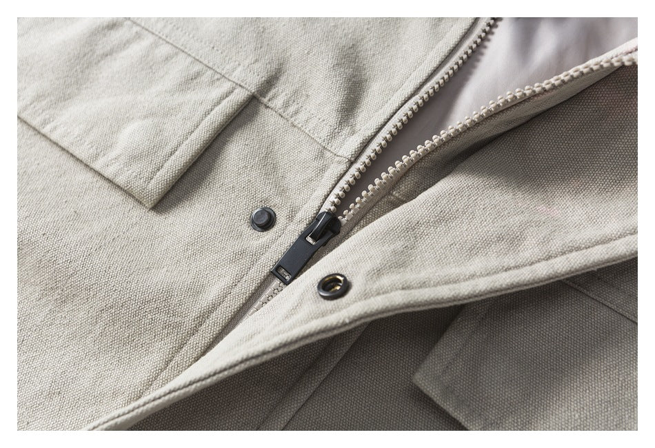 Close-up of a light beige jacket showing its dark zipper, snap buttons, and overlapping front flap.