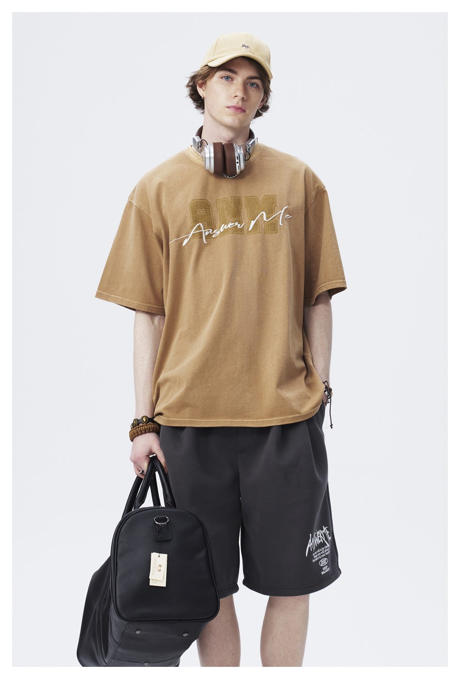 Front view of a model wearing a tan graphic T-shirt with charcoal shorts and a beige cap.
