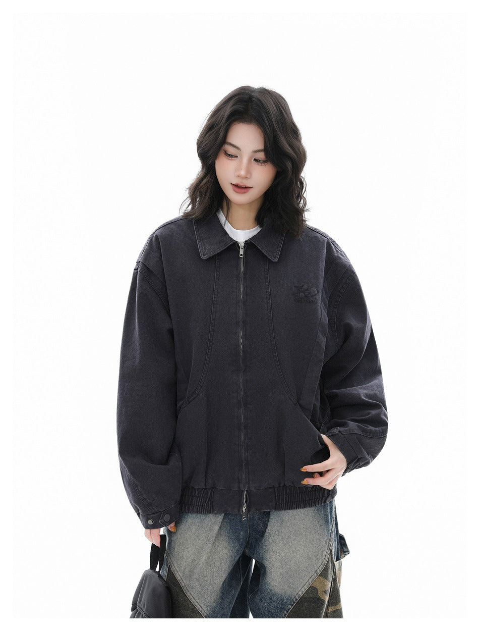 Model wearing a charcoal zip-front jacket with a pointed collar, curved pockets, and gathered hem.