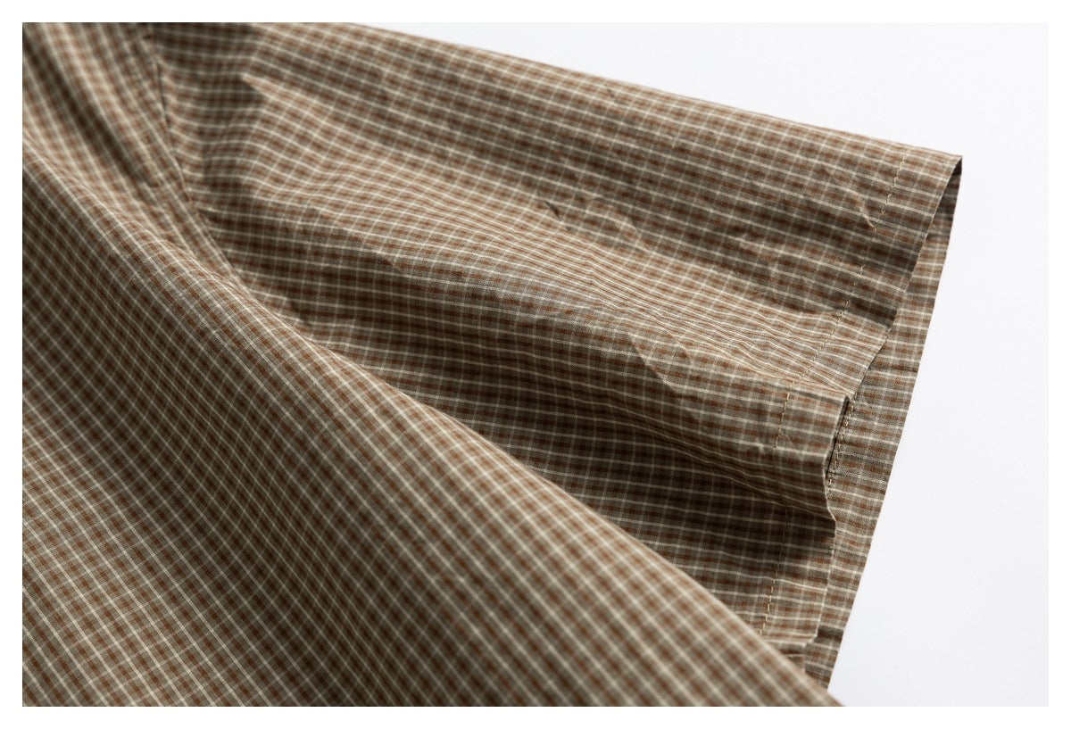 Close-up of a brown and cream checked shirt sleeve and stitched edge.