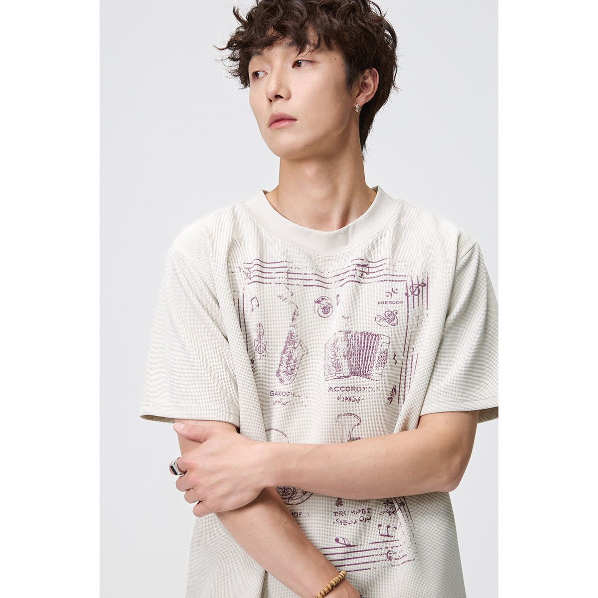 Model wearing an ivory short-sleeve T-shirt with a large burgundy musical-instrument graphic.