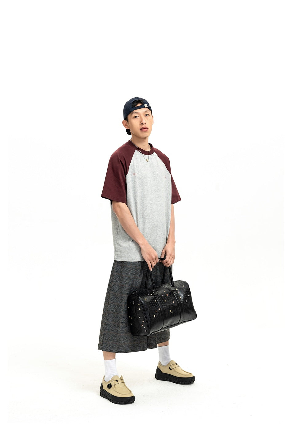 Three-quarter view of a model wearing a gray and burgundy raglan T-shirt with plaid shorts.