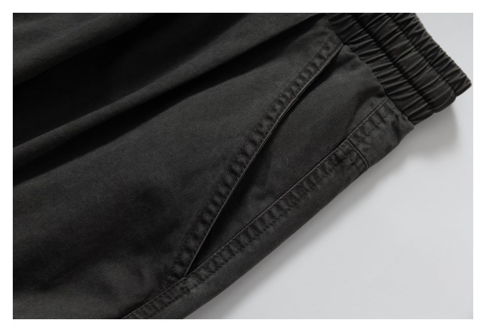 Close-up of charcoal pants showing a slanted side pocket, stitching, and elastic waistband.