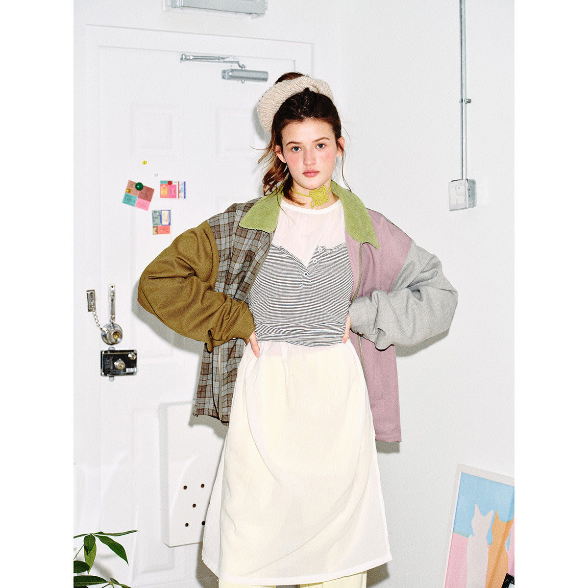 Model wearing a patchwork jacket with a plaid panel, olive and gray sleeves, dusty pink panel, and green collar.