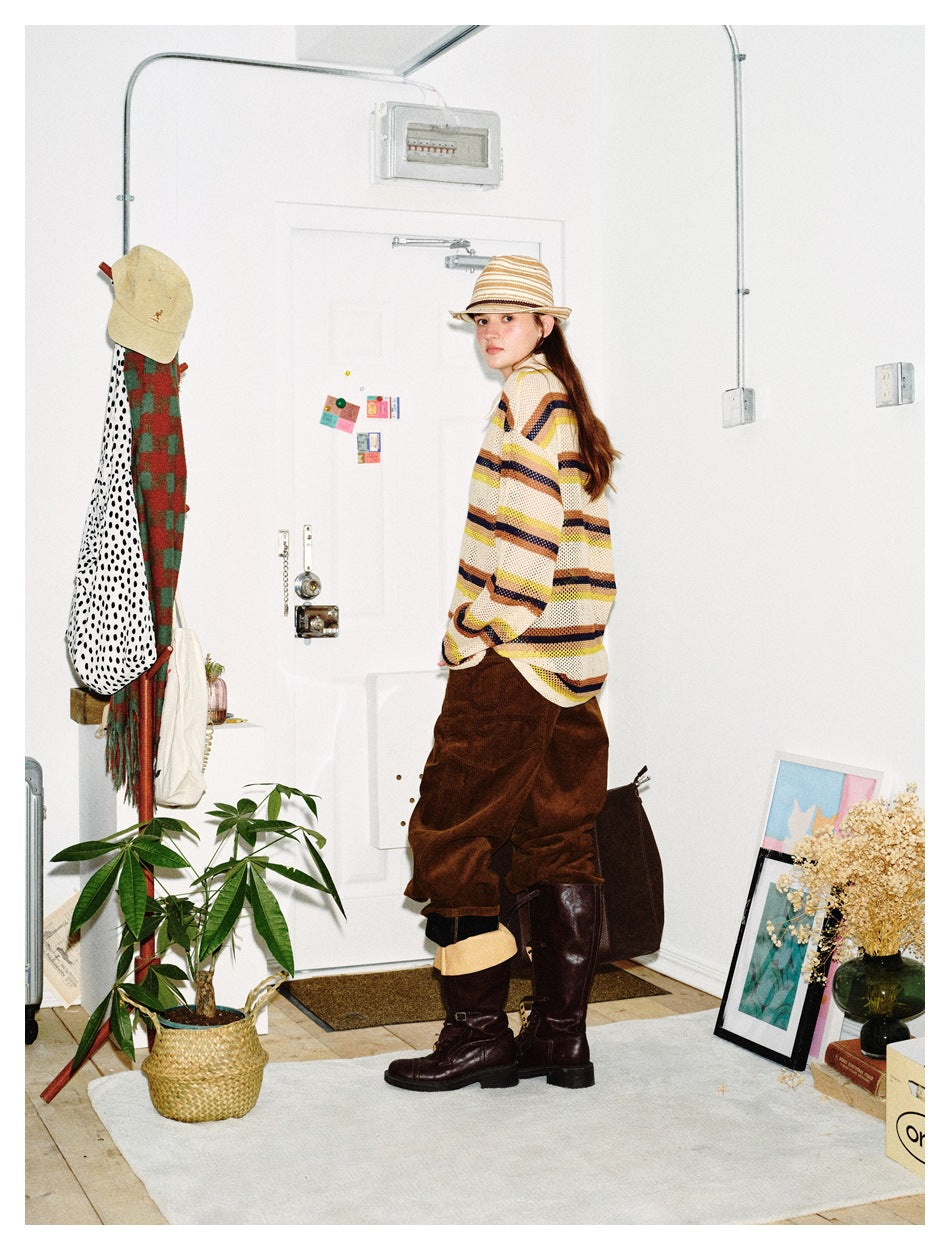 Model in a striped cream sweater, shown from the side and back with brown trousers and tall boots.