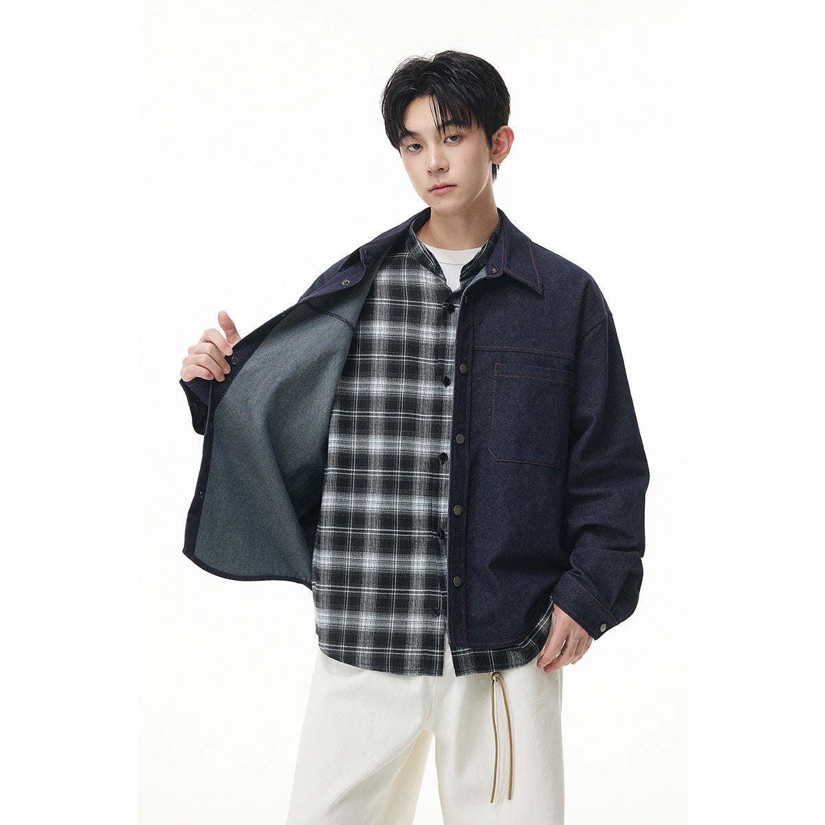 Model opens a dark indigo button-front jacket to show its lighter interior and black-and-white plaid shirt lining.