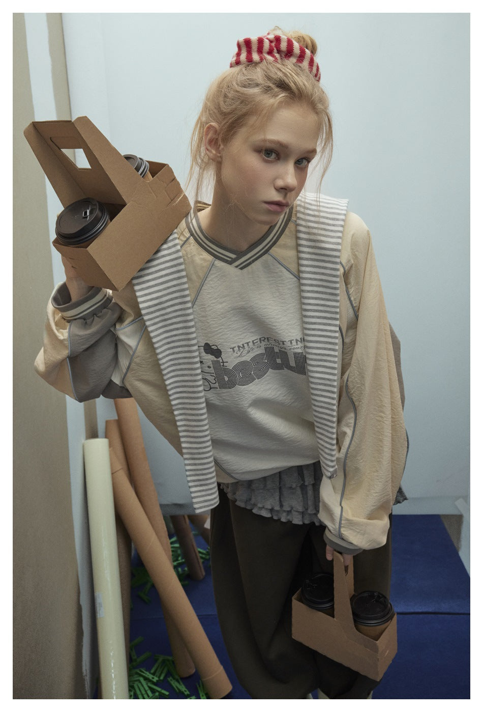 Close view of a model wearing a cream sweatshirt with a printed chest graphic, striped neckline and gray piping.