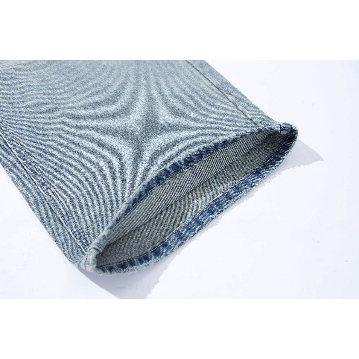 Close-up of a turned-up hem on light-wash blue jeans, showing the denim and stitching.