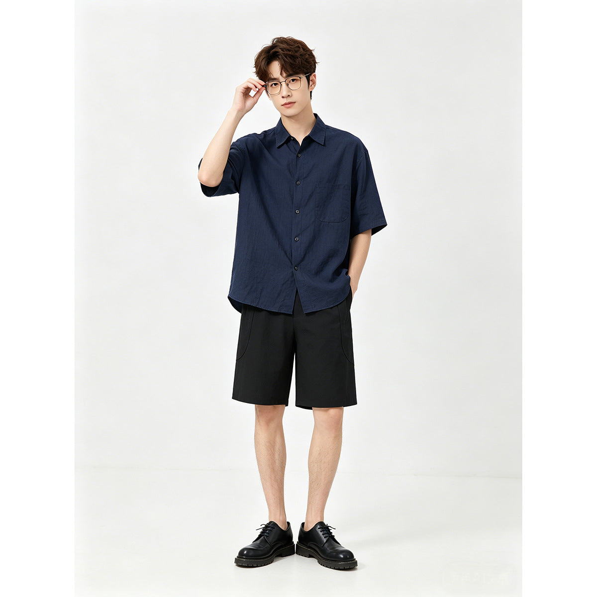 Model wearing a navy short-sleeve button-up shirt with a chest pocket and black shorts.