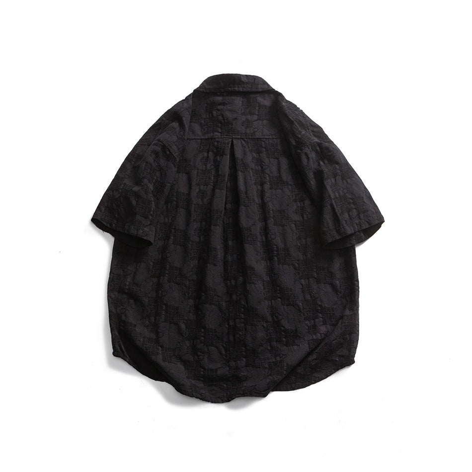 Back view of a black short-sleeve button-up shirt with a subtle textured pattern and center pleat.