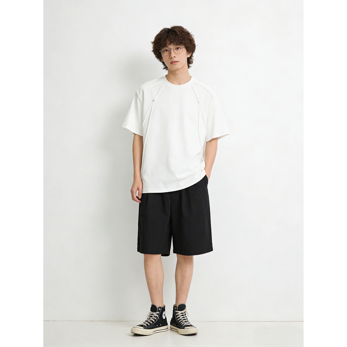 Standing model wearing an oversized white short-sleeve tee with curved front panels and small snaps.