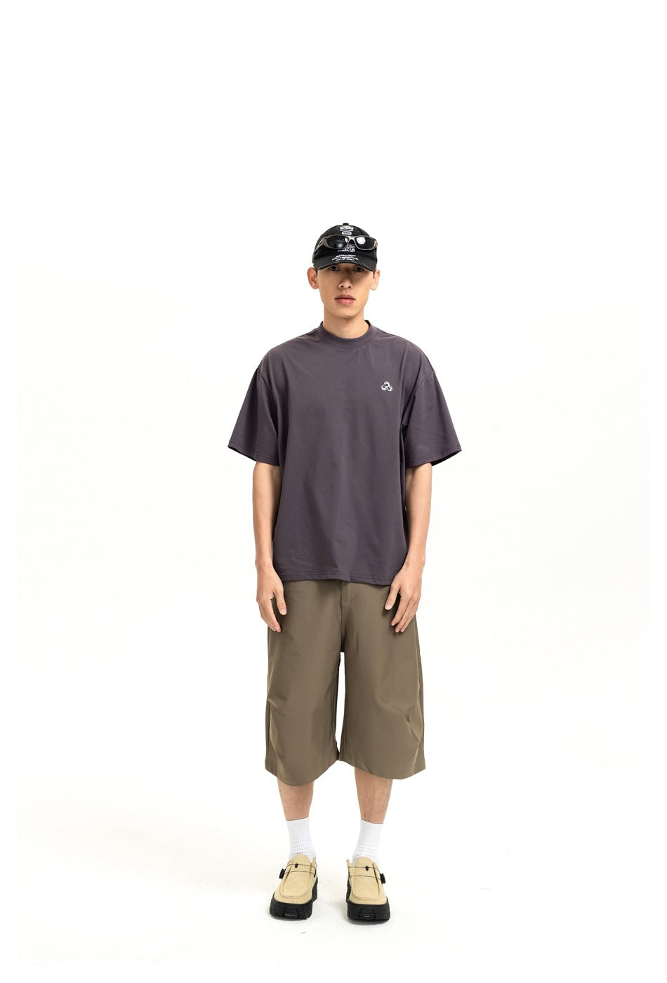 Model wearing khaki-brown wide-leg knee-length shorts with a gray T-shirt, cap and beige shoes, front view