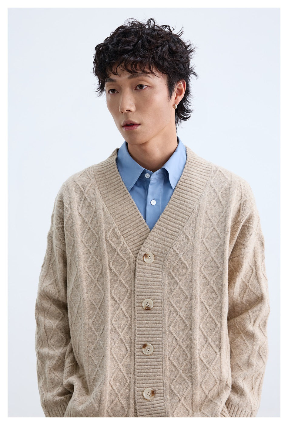 Close-up of the beige cardigan's diamond cable-knit pattern, ribbed V-neck placket, and buttons on a model.