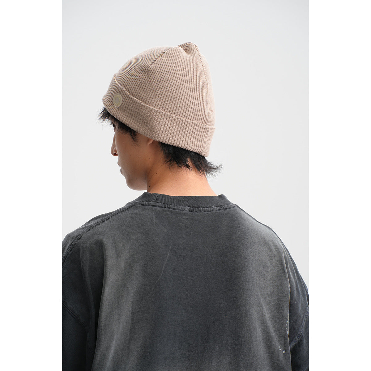 Close-up from behind showing the charcoal T-shirt neckline and upper back with a beige rib-knit beanie.