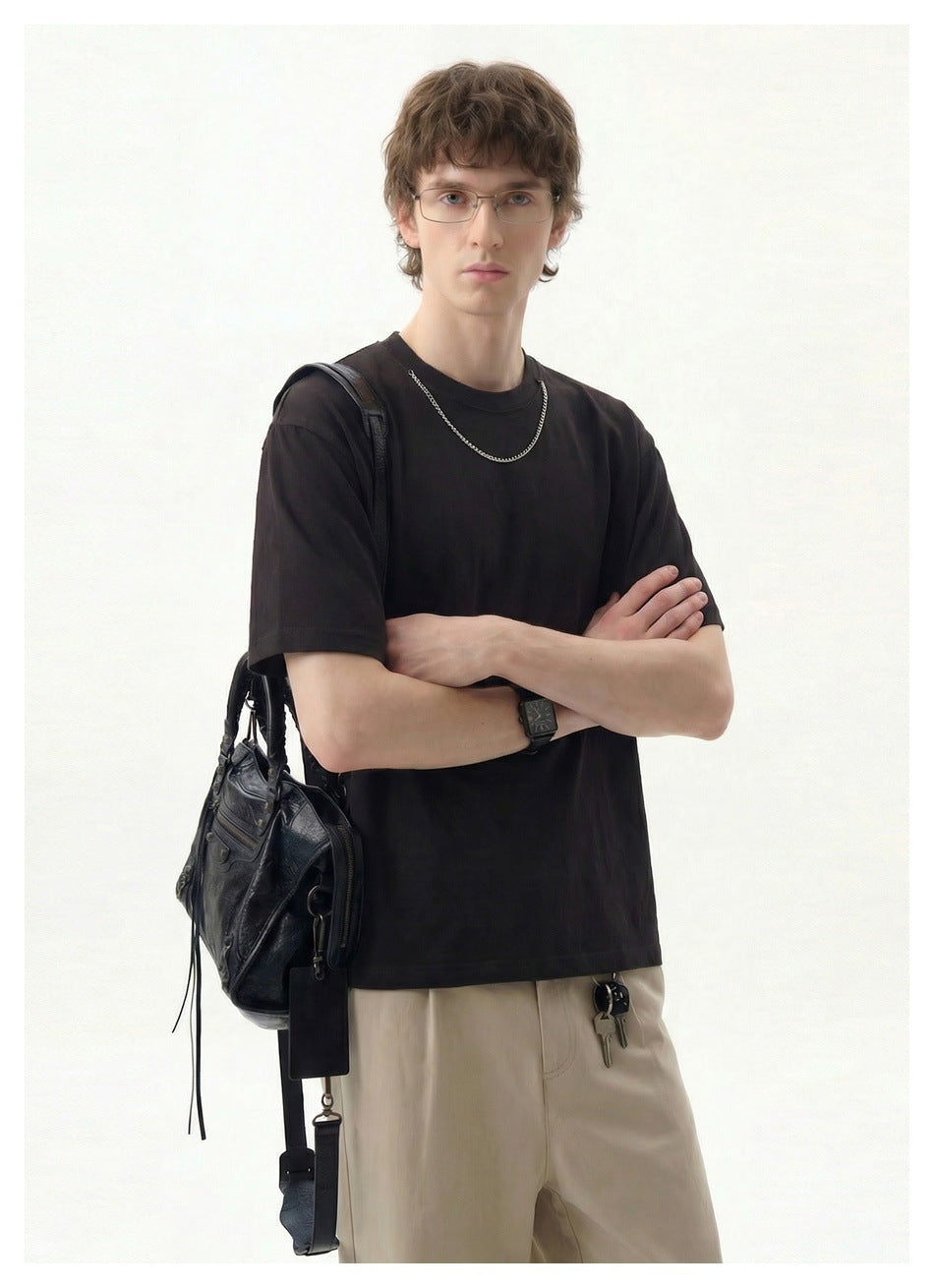 Model wearing a plain black short-sleeve crew-neck T-shirt with beige trousers and a black shoulder bag.