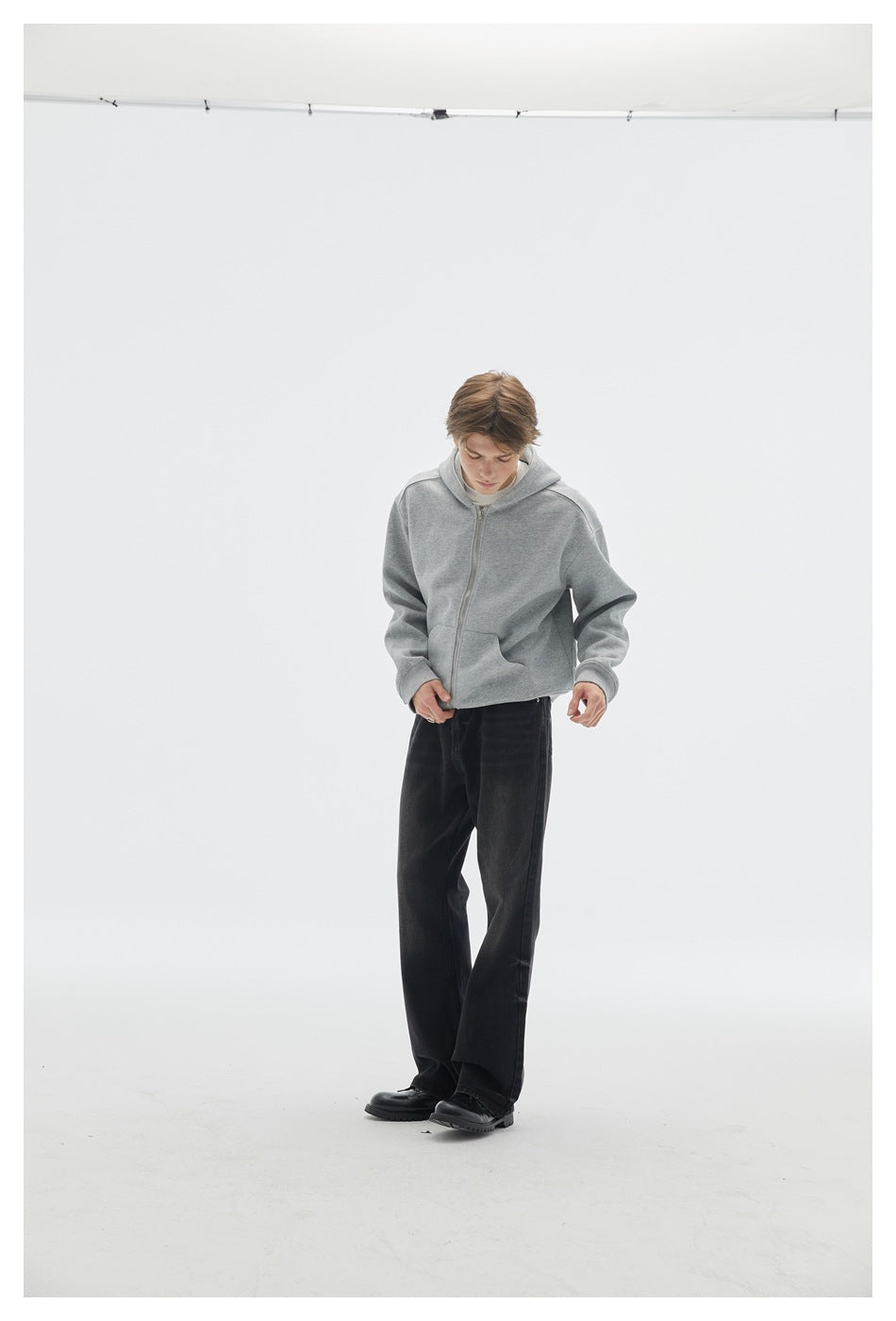 Model looking down while wearing a light gray zip-front hoodie with a hood and front pockets.