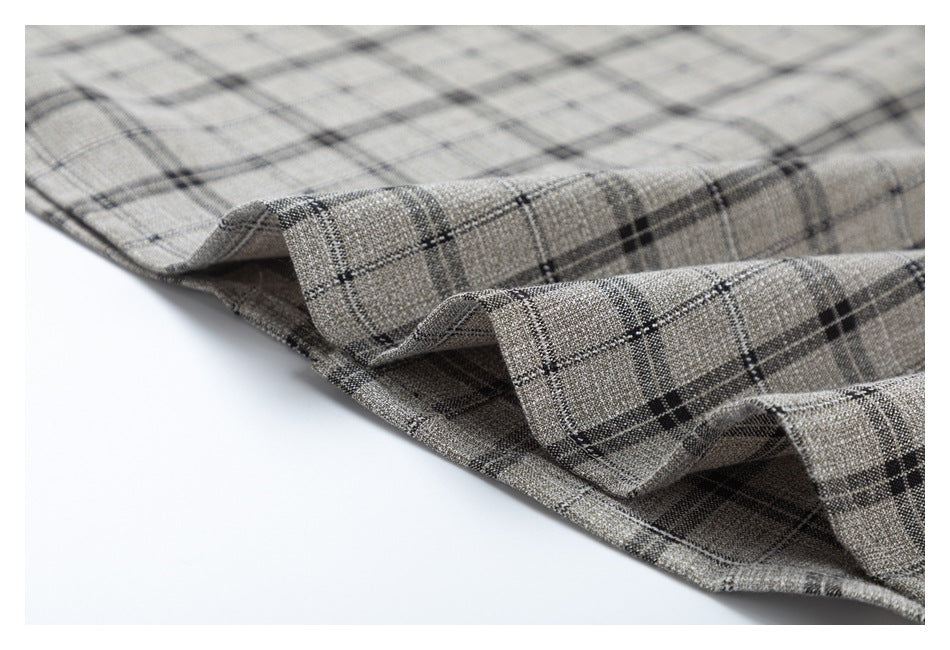 Close-up of a folded hem on gray-beige plaid fabric with dark intersecting lines.