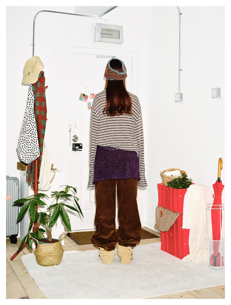 Back view of a model wearing a gray striped long-sleeve top, purple waist wrap, and brown trousers.