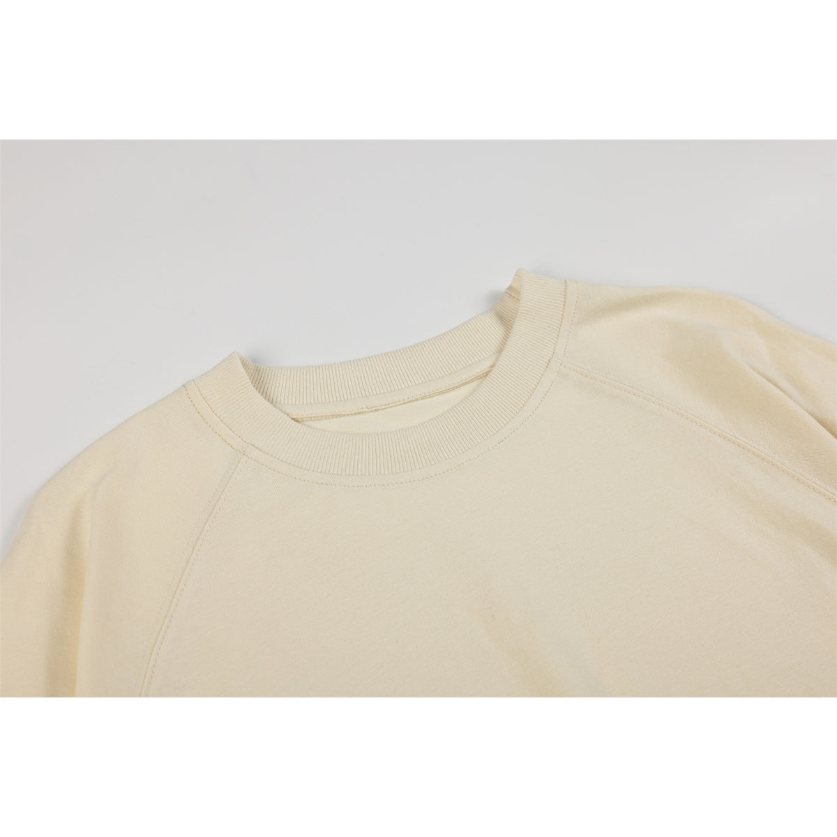 Close-up of an ivory sweatshirt showing its ribbed crew neckline and raglan shoulder seams.