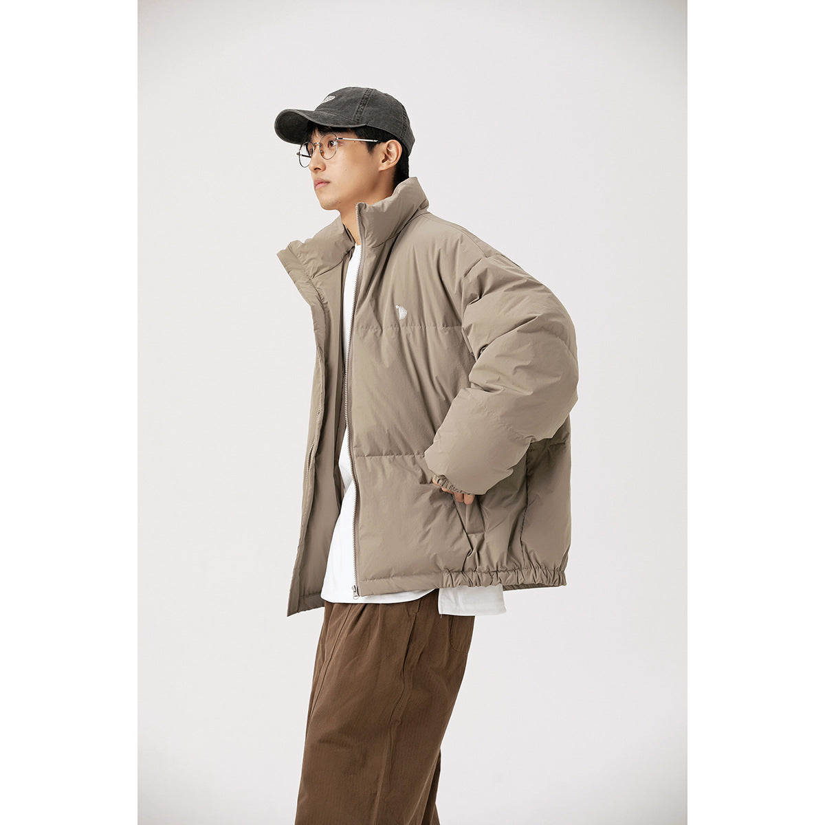 Side view of a model wearing an open taupe puffer jacket with a high collar.