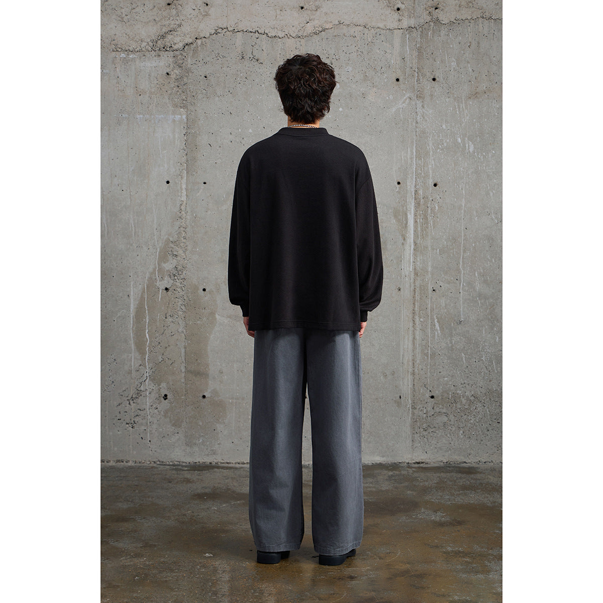 Back view of a model wearing a plain black oversized crewneck and wide gray trousers.