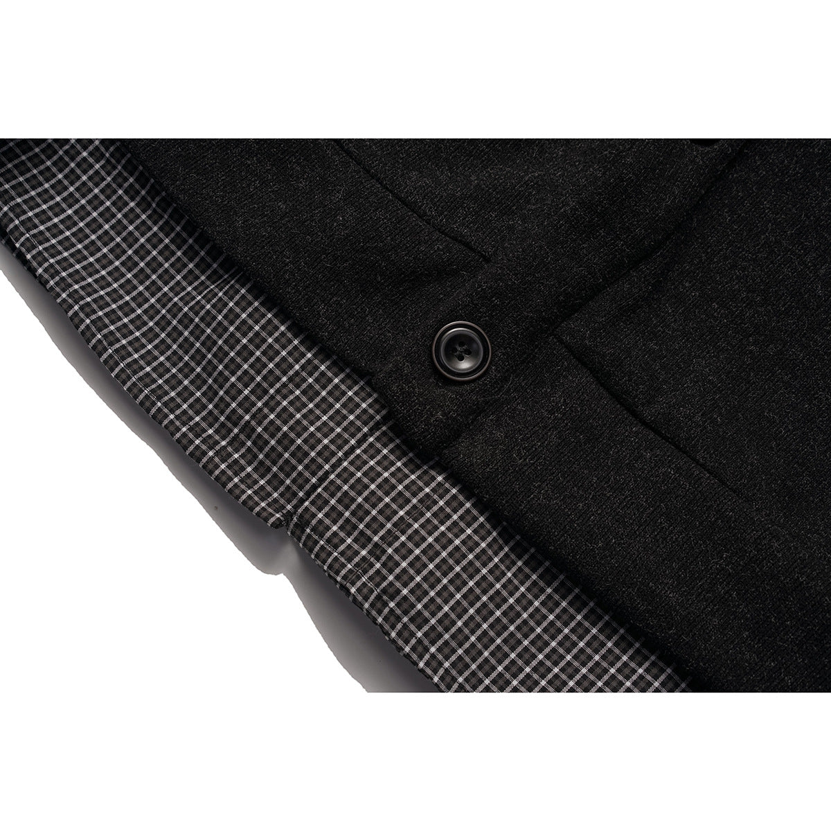 Close-up of a black cardigan button and gray checked fabric peeking from beneath it.