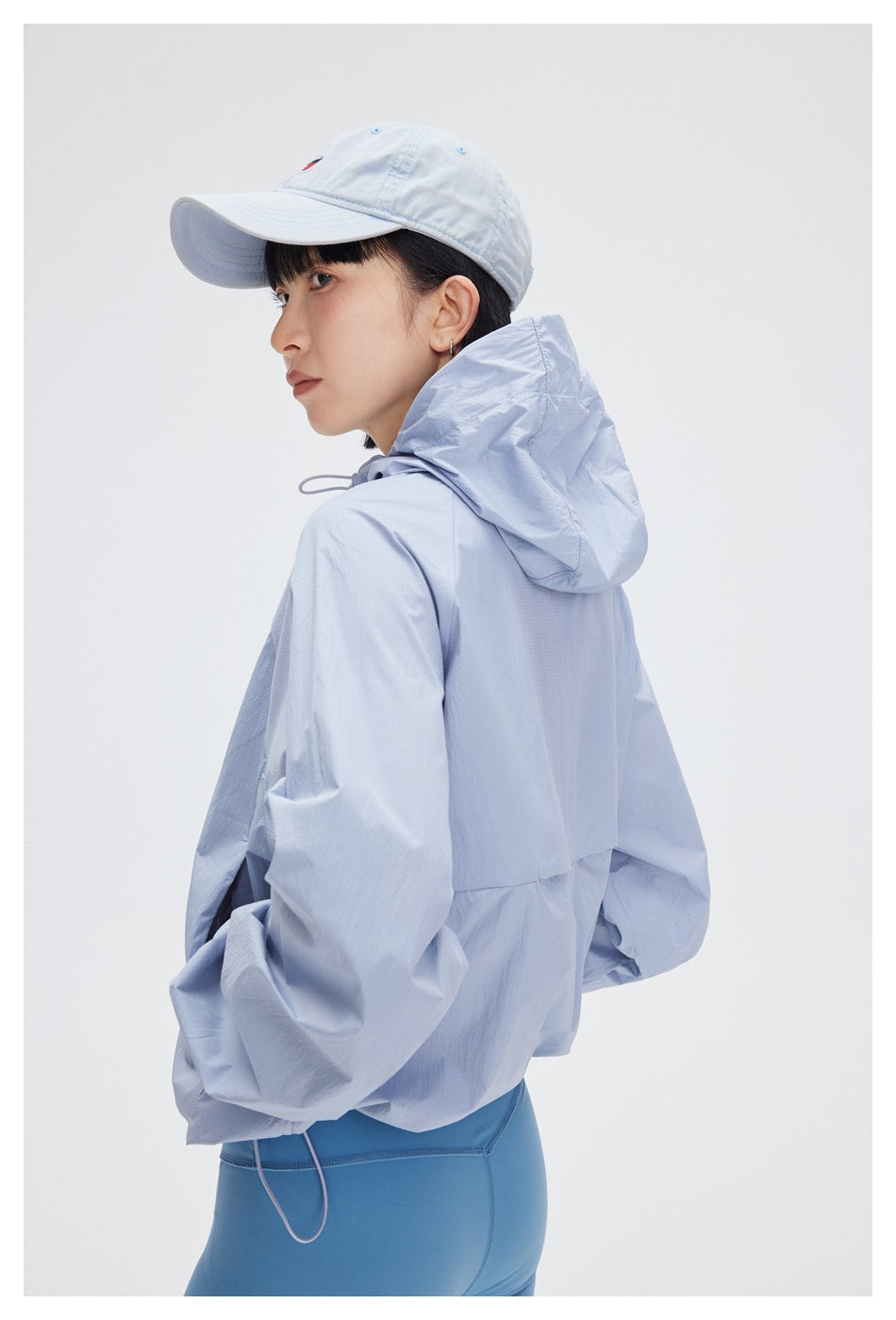 Rear three-quarter view of a woman wearing a pale blue hooded jacket and blue leggings.