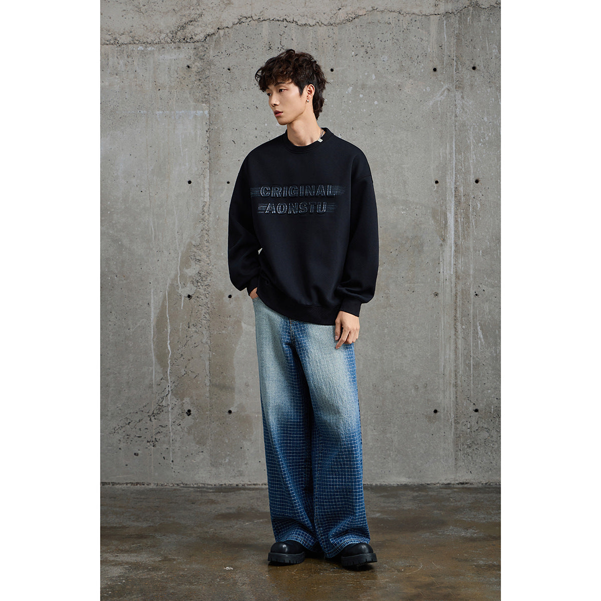 Full-length model wearing a black graphic crewneck sweatshirt, blue plaid wide-leg trousers, and black shoes.