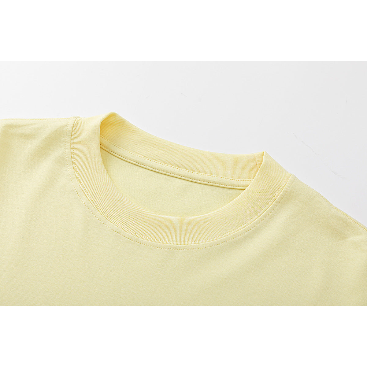 Close-up of a pale yellow shirt's ribbed crew neckline and shoulder seams.