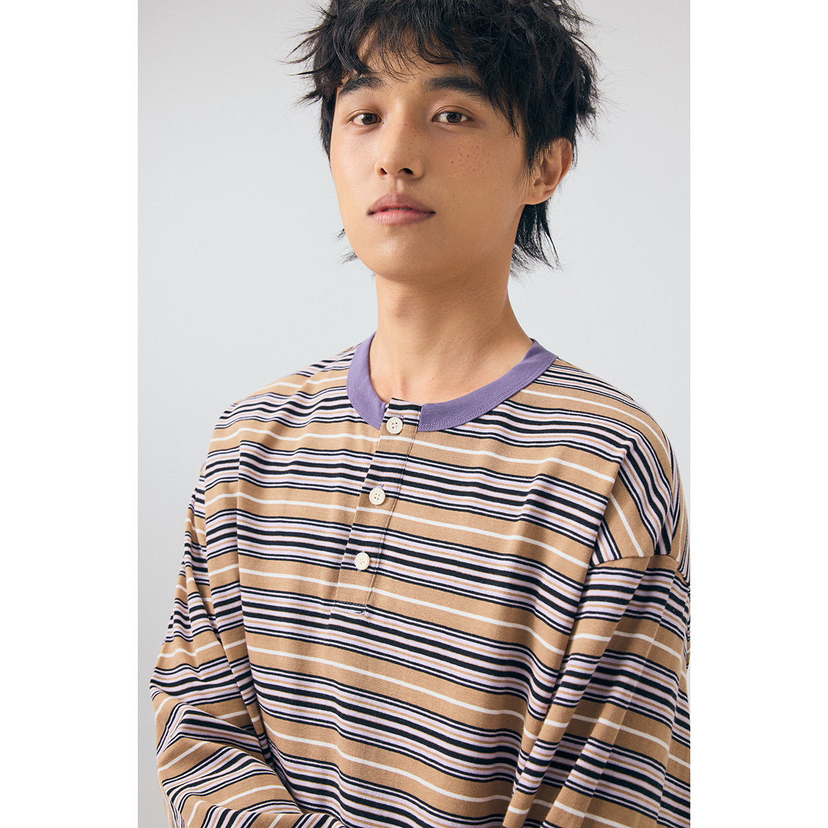 Close-up of a model wearing a tan, navy and white striped henley with a lavender collar and three-button placket.