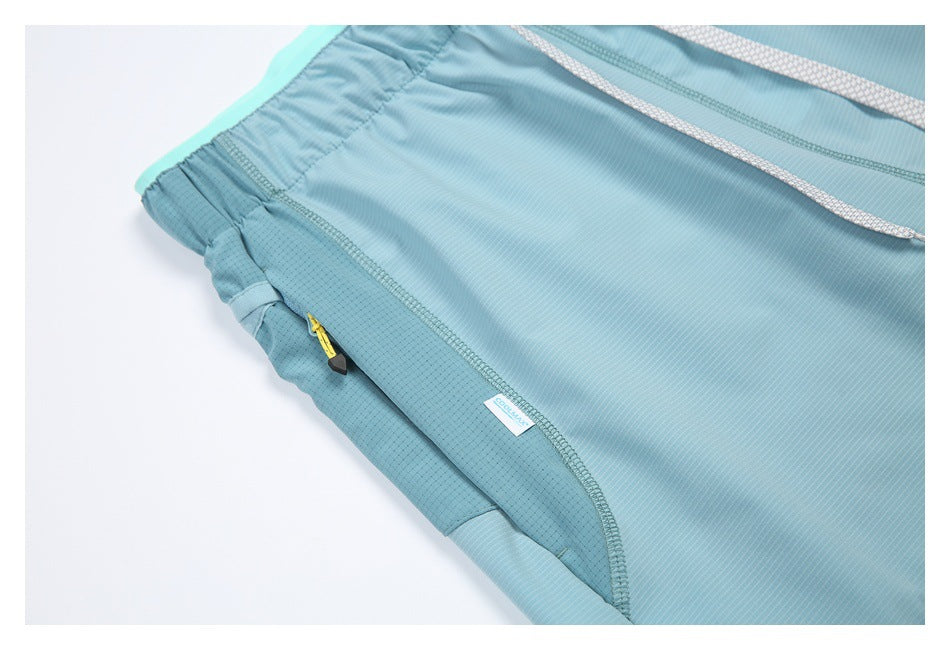 Close-up of blue shorts showing the elastic waistband, white drawcords, and a zip pocket with a yellow pull.