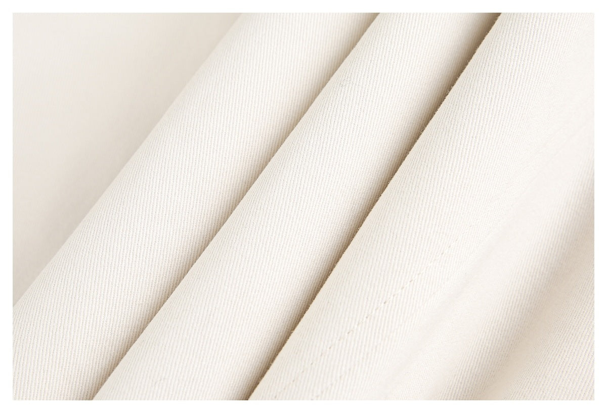 Close-up of folded ivory garment fabric with fine diagonal texture and a stitched seam.