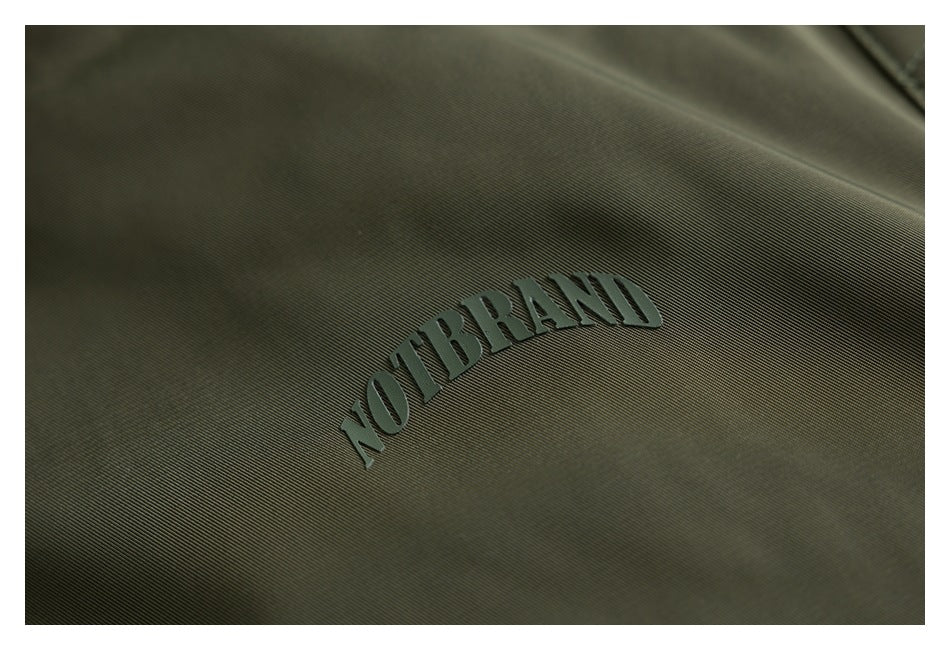 Close-up of dark olive fabric with raised “NOT BRAND” lettering.