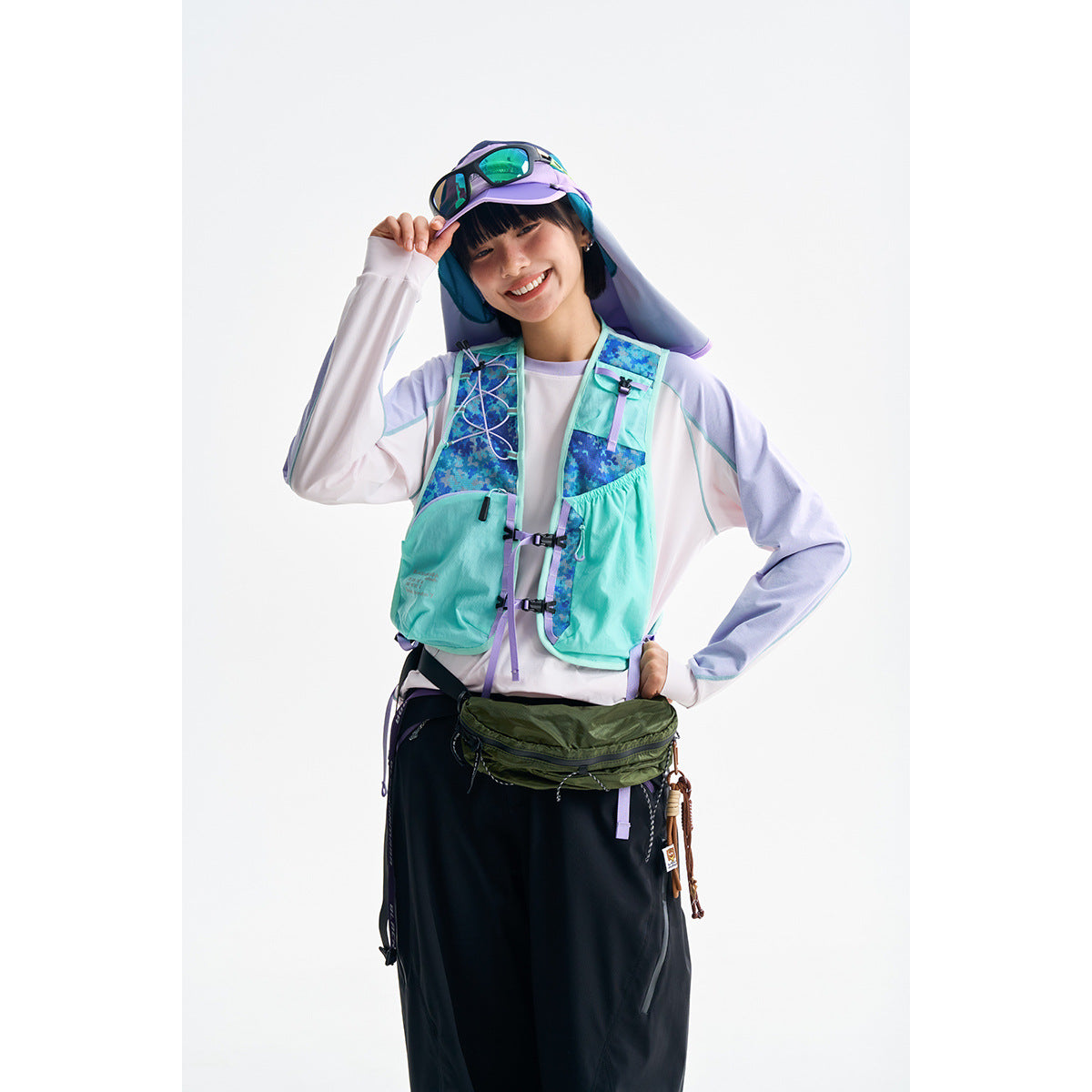 Model wearing a turquoise and blue patterned running vest with lavender straps over a white top.