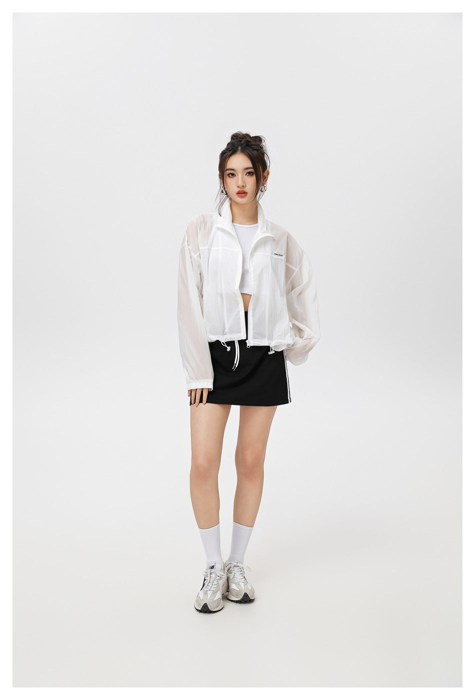 Model wearing a sheer white cropped zip jacket with a stand collar and drawcord hem, paired with a black mini skirt.
