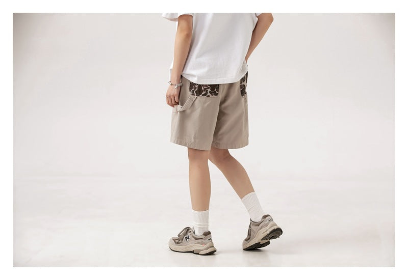 Cropped angled back view of a model wearing beige shorts with dark patterned back pockets.