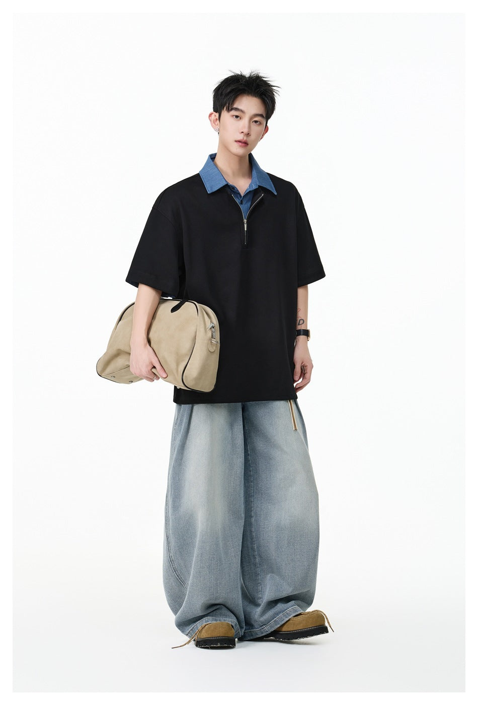 Model wearing the black half-zip polo top with blue collar, holding a beige bag, with wide light-wash jeans