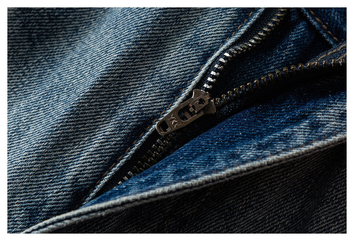 Close-up of a metal zipper on dark blue denim, showing the teeth, slider and surrounding seams.