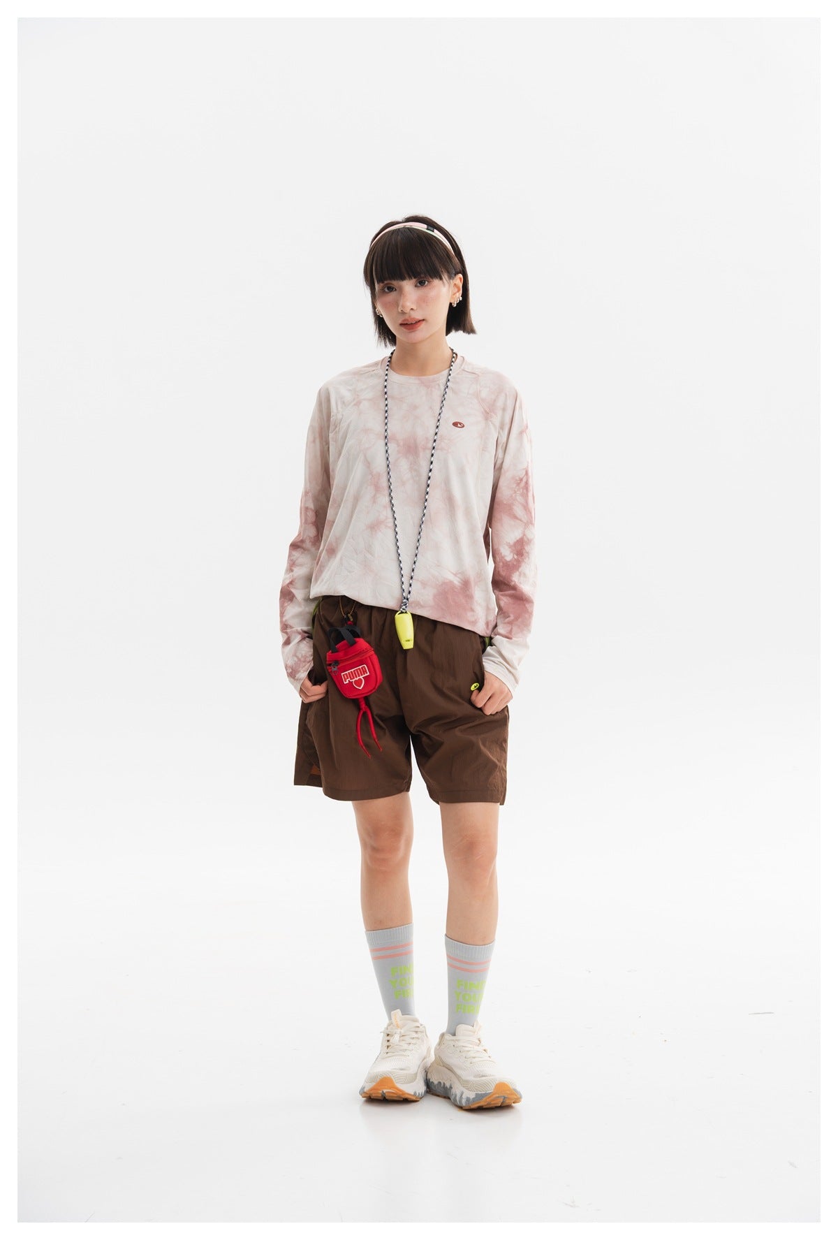 Model wearing a cream and dusty-pink tie-dye long-sleeve crewneck shirt with brown shorts, front view.