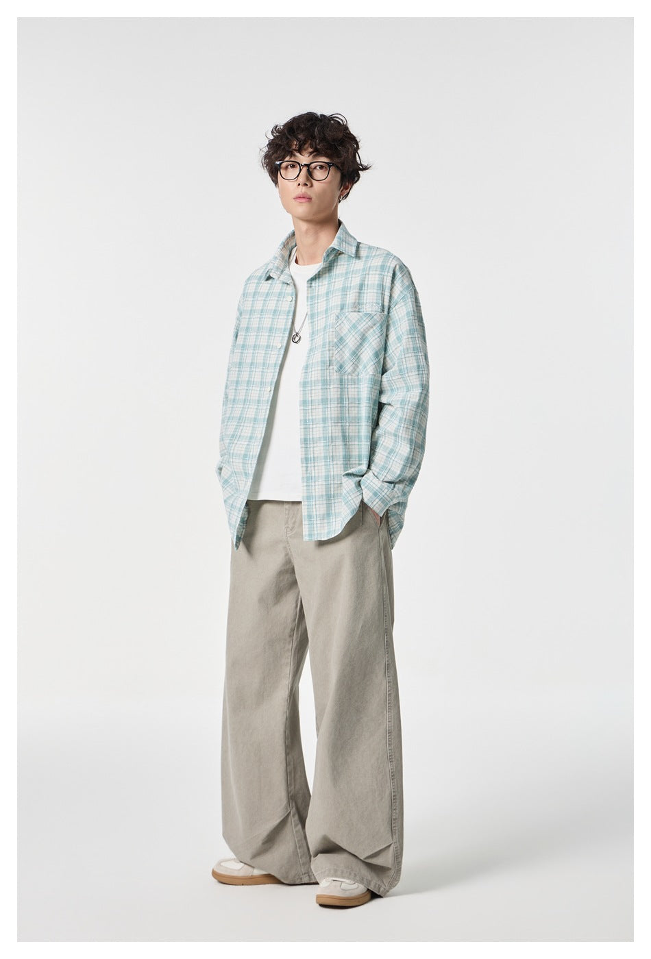 Model wearing an open aqua and white plaid button-up shirt over a white tee with loose gray trousers.