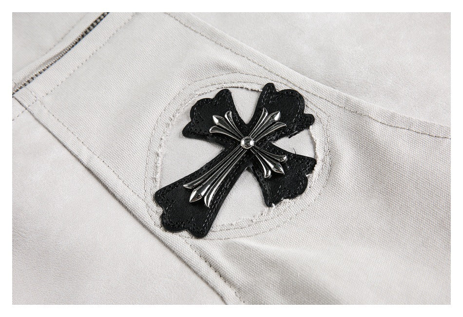 Close-up of a black cross-shaped appliqué with a silver-tone embellishment on the light gray jacket.