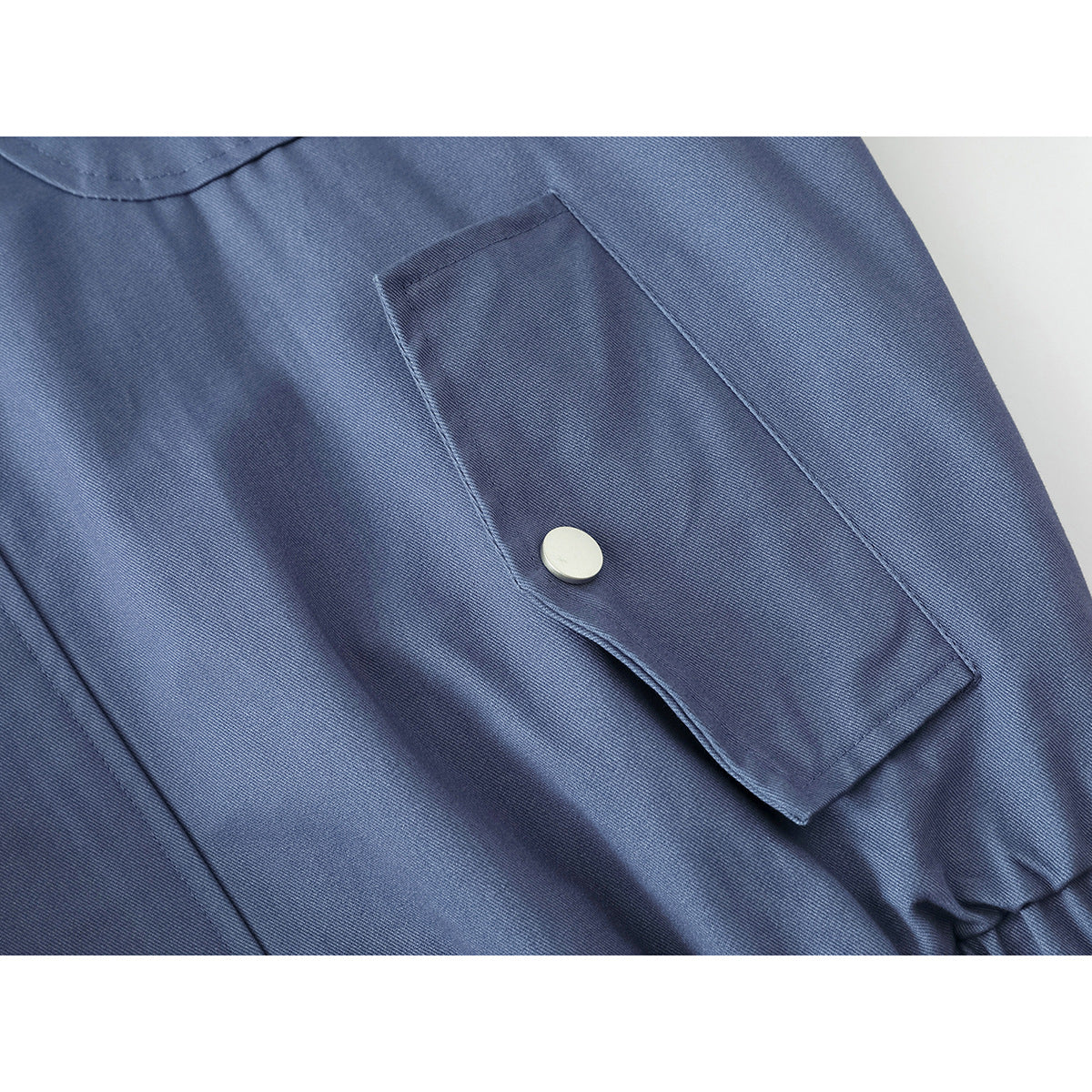 Close-up of a blue jacket pocket flap with a silver snap fastener.